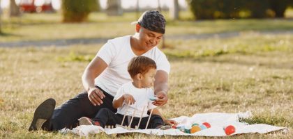 A joyful father and son playing together on a blanket in a sunlit park.