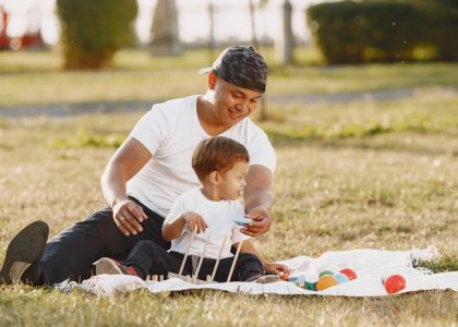A joyful father and son playing together on a blanket in a sunlit park.