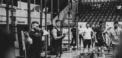 Black and white image of a fitness competition showcasing athletes and weights in a gym setting.