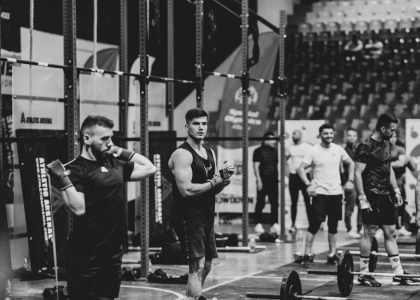 Black and white image of a fitness competition showcasing athletes and weights in a gym setting.